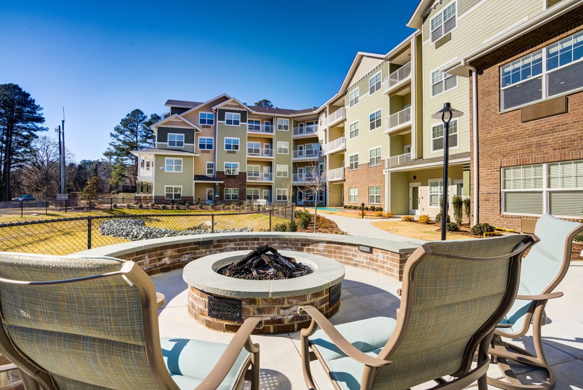 A scenic view of a modern apartment complex featuring a shared outdoor seating area with a fire pit.
