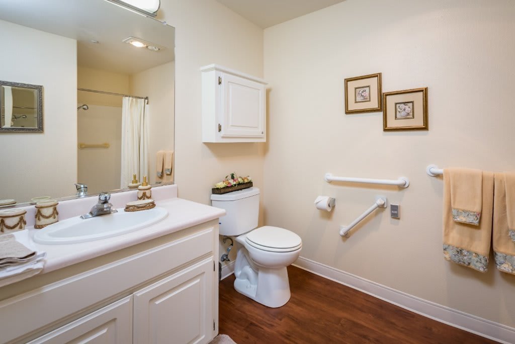 A clean and well-organized bathroom with a toilet, sink, mirror, and wooden flooring.