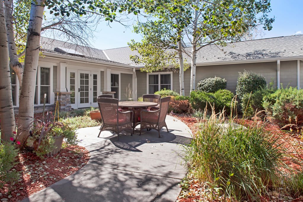 A serene courtyard with patio furniture surrounded by lush greenery on a sunny day.