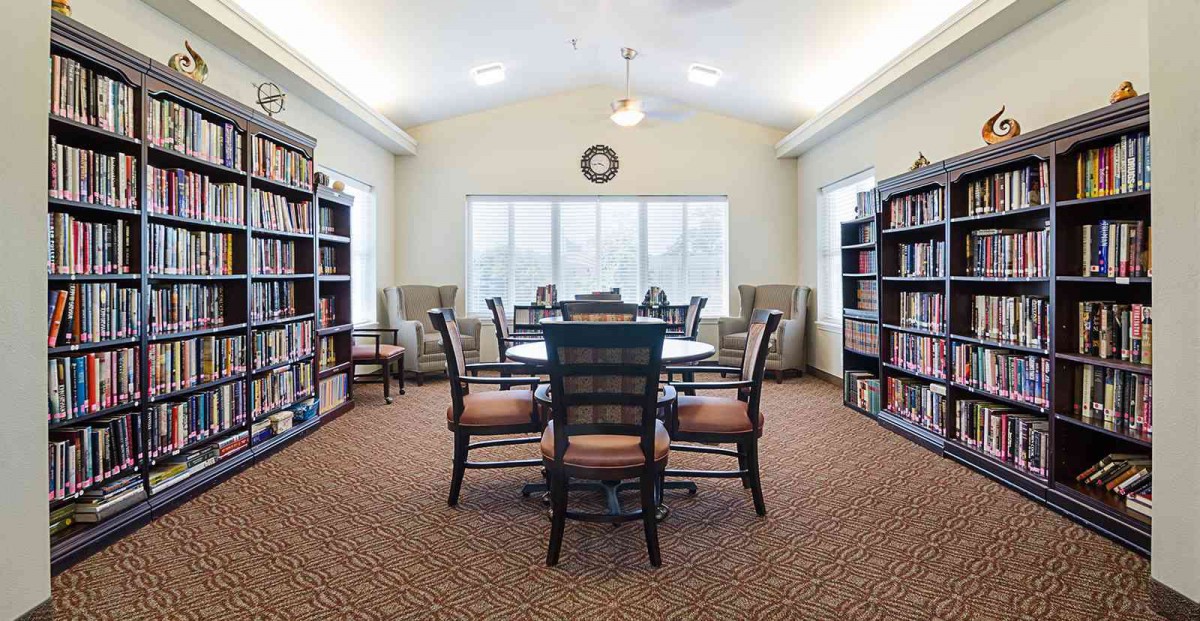 A cozy library with a central table surrounded by bookshelves and seating.