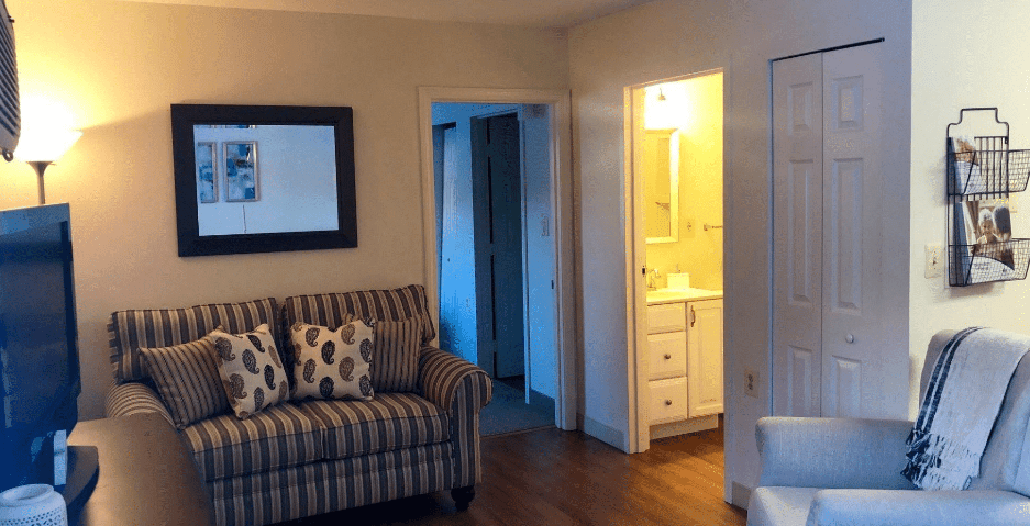 A cozy living room with a striped couch, wooden flooring, and an adjacent bathroom.