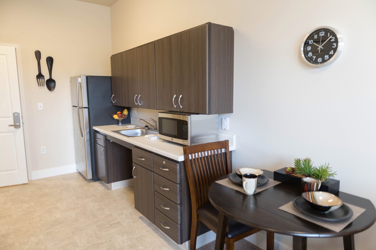 A modern kitchen with dark wood cabinets, a small dining table, and essential appliances.