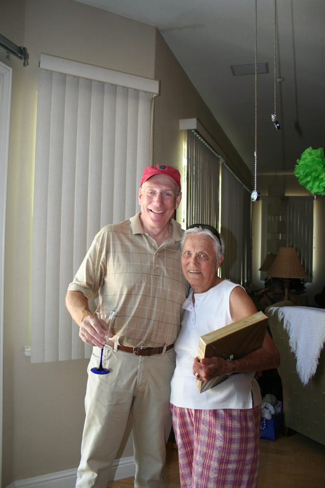 Two people posing indoors, one holding a wine glass and wearing hats.