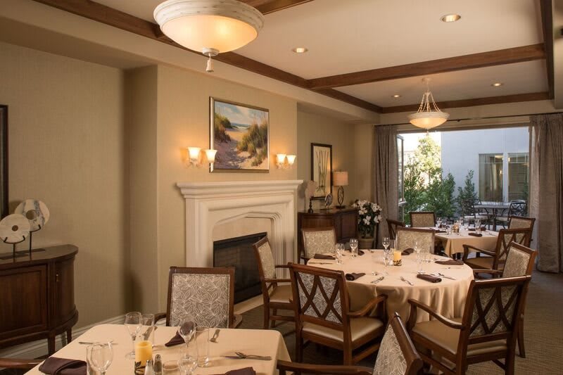 An elegant dining room with neatly arranged tables and chairs, featuring a fireplace and artwork on the wall.