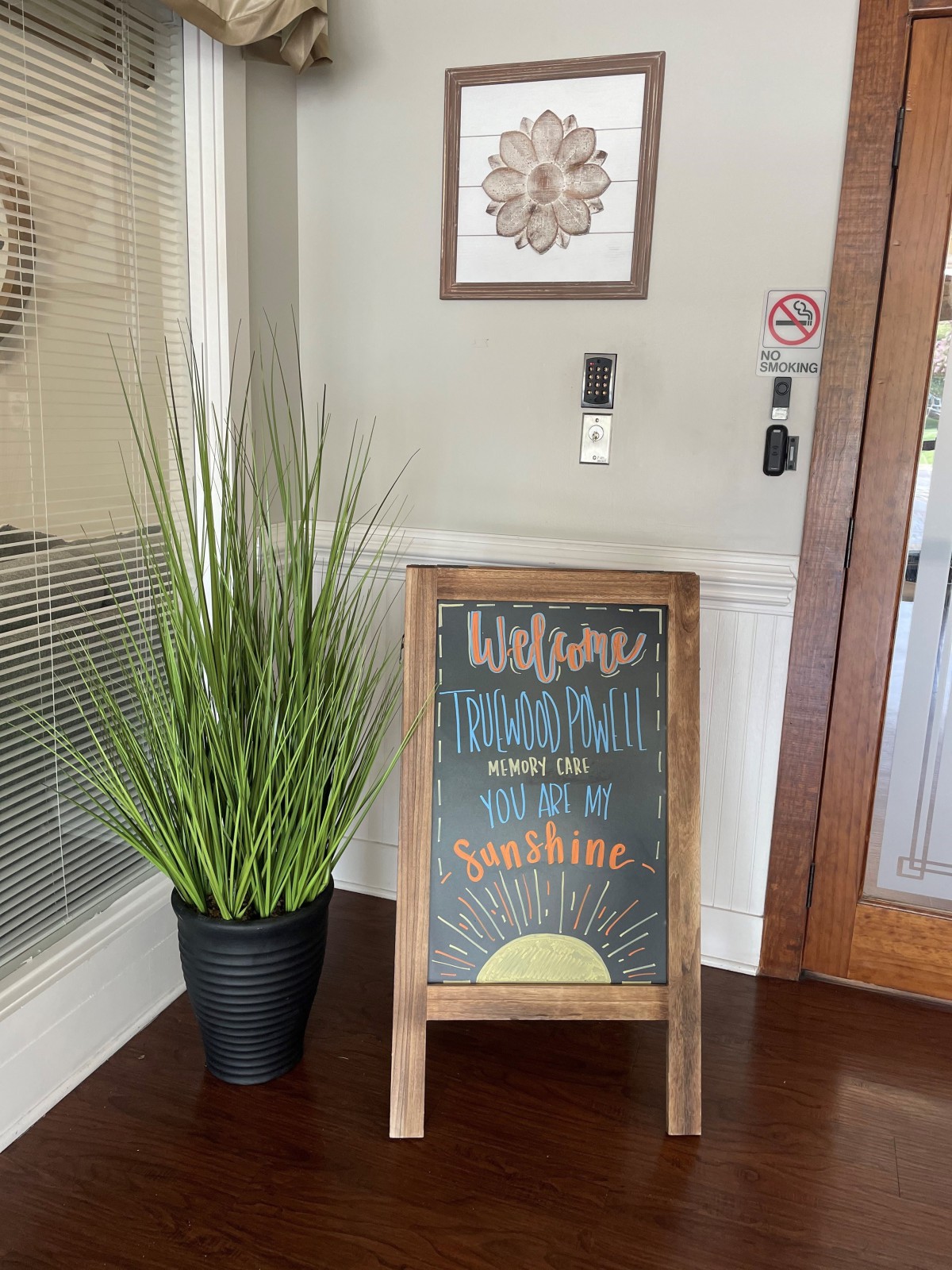 A welcoming chalkboard sign with a plant beside it at an entrance.