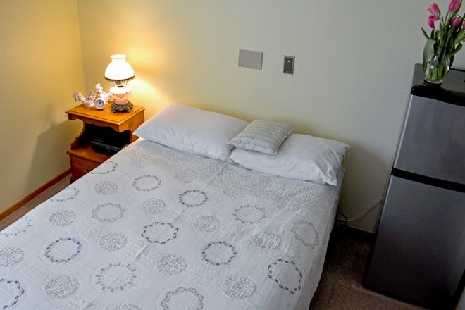 A cozy bedroom with a neatly made bed, soft lighting from a lamp on the nightstand, and simple decor.