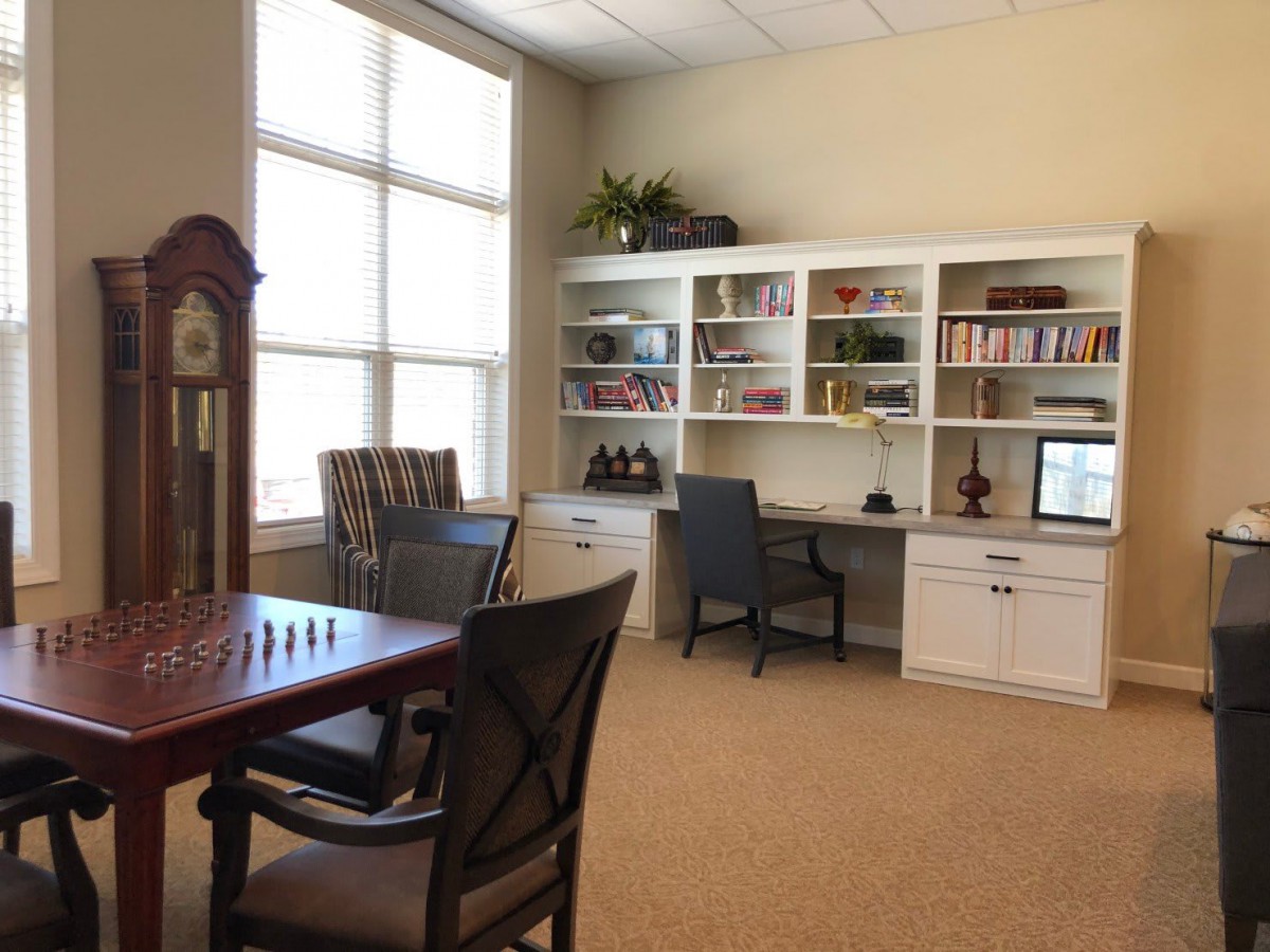 A cozy office with a desk, bookshelf, and a chessboard by the window.