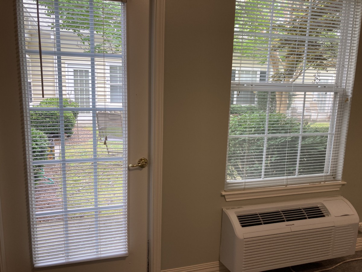A room interior showing a door and window with blinds, offering a view of the outside.
