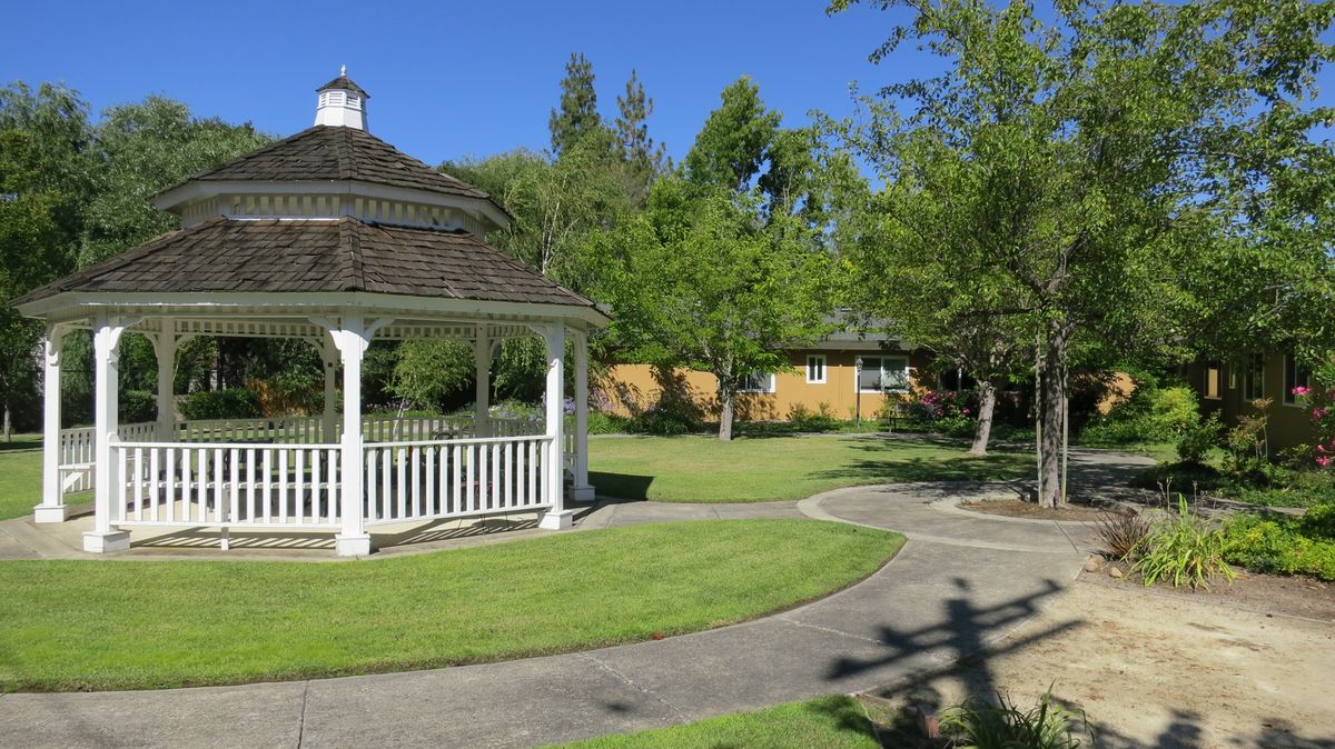 A peaceful park scene featuring a white gazebo surrounded by lush green lawns and trees.