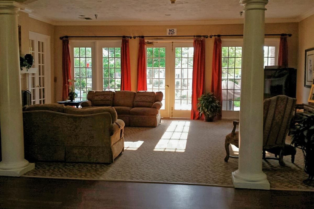 A cozy living room with large windows and red curtains, featuring a comfortable sofa and natural lighting.