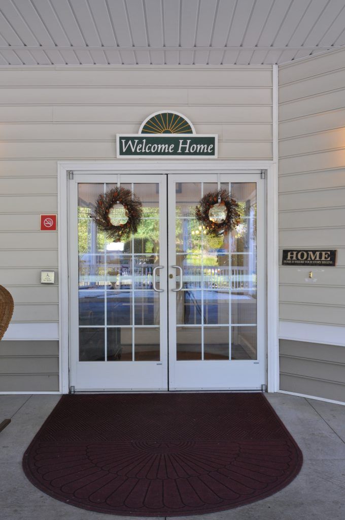 A double glass door entrance adorned with wreaths and a 'Welcome Home' sign above.