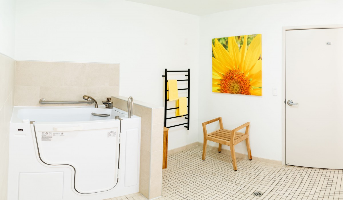 A wheelchair-accessible bathroom with a bathtub and sunflower painting on the wall.