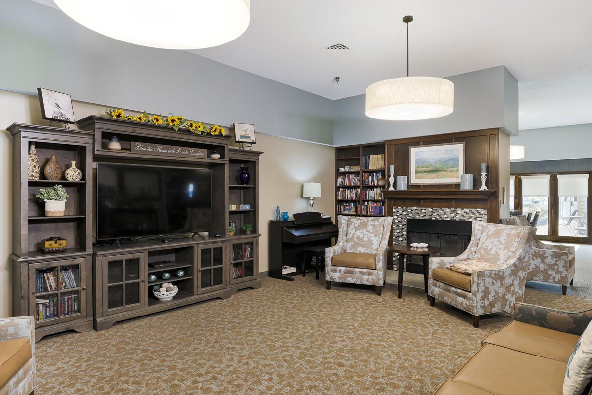 A cozy living room featuring a large television, entertainment center, bookshelves, two patterned chairs, and a piano.