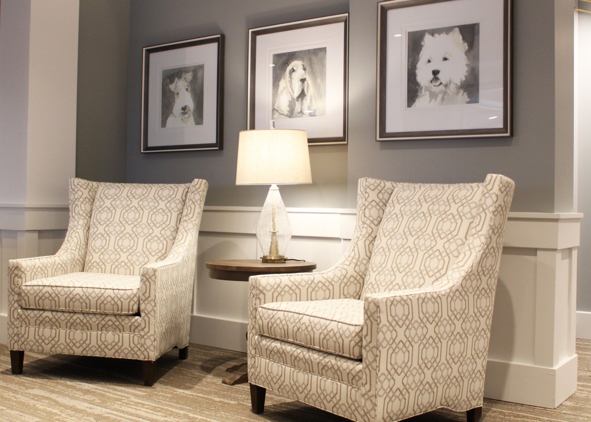 A cozy seating area with two patterned chairs, a lamp, and framed artwork on the wall.
