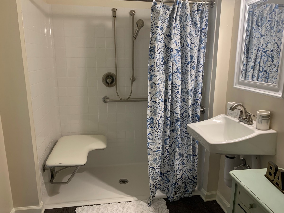 A bathroom featuring an accessible shower with a folding seat and grab bar.