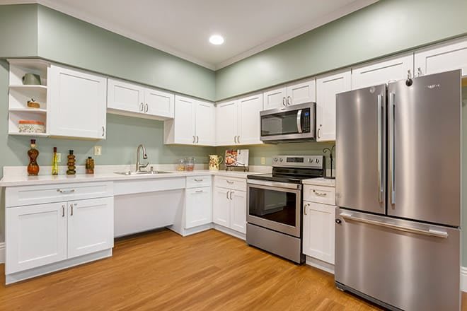 A modern kitchen featuring white cabinets, stainless steel appliances, and warm wood flooring.