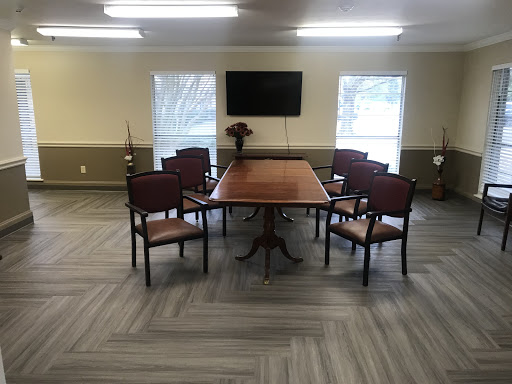 A spacious conference room featuring a large table surrounded by chairs, with a television mounted on the wall and natural light coming through windows.