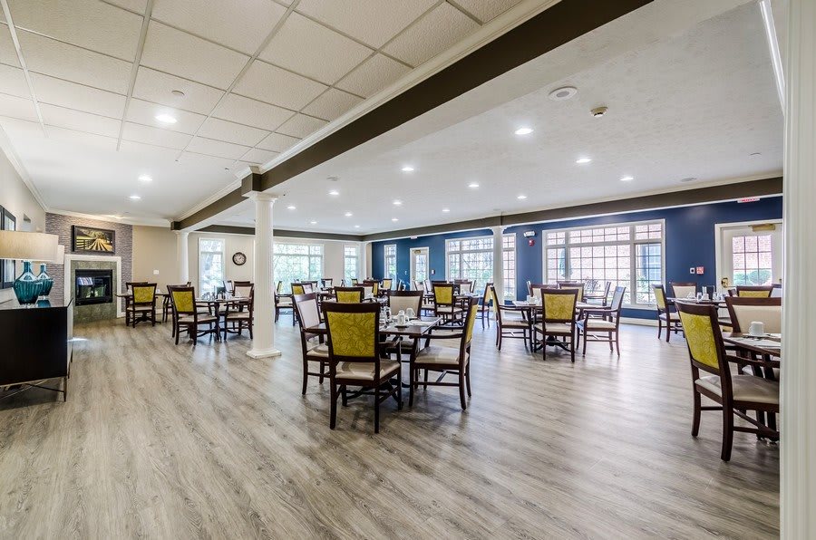 A spacious modern dining room with multiple tables and chairs, featuring large windows.