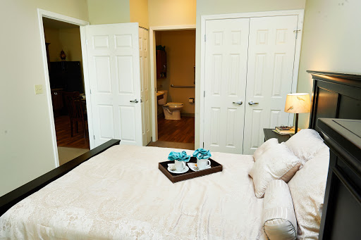 A cozy bedroom featuring a neatly made bed with a tray of cups, leading to a bathroom and closet area.