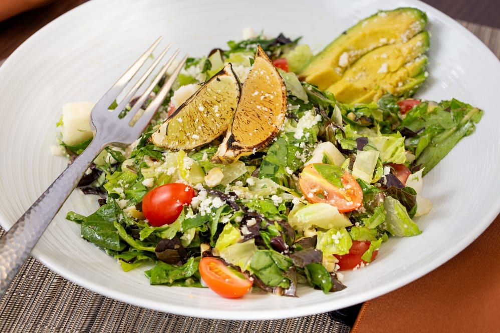 A fresh and colorful salad featuring avocado, cherry tomatoes, lime slices, and mixed greens.
