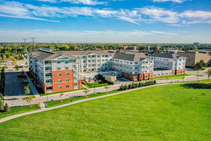 Aerial view of a modern apartment complex surrounded by green lawns under a clear blue sky.