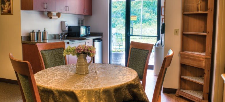A cozy kitchen and dining area with a round table, floral centerpiece, and view to the outdoors.