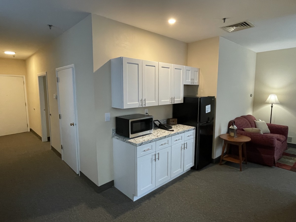 A small kitchen area with white cabinets, a microwave, and a refrigerator in a room.