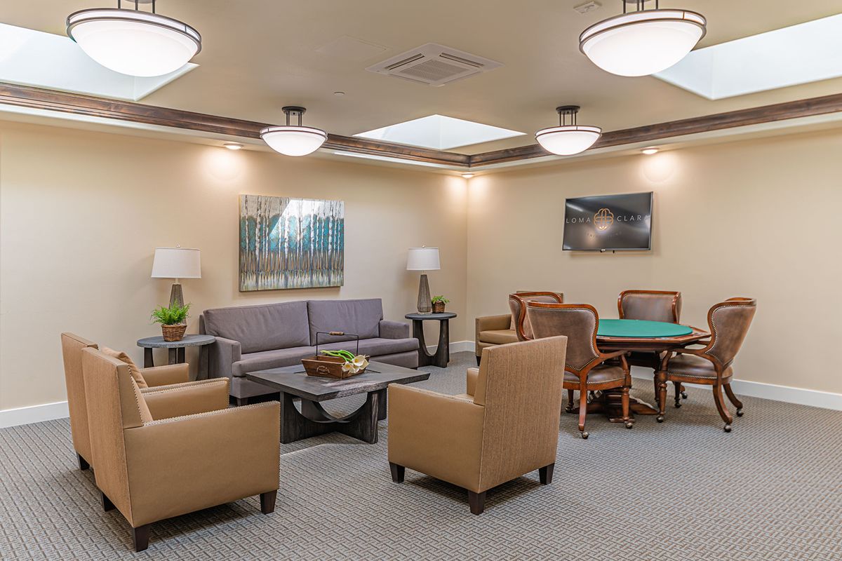 A modern lobby seating area featuring comfortable sofas, armchairs, and a card table under soft lighting.