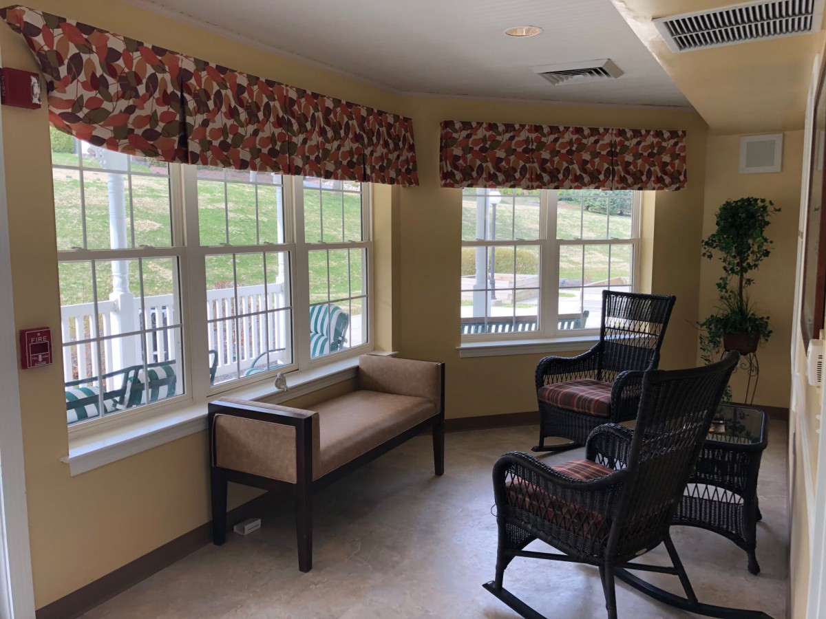 A cozy waiting area with large windows, allowing natural light to fill the space, featuring a bench and wicker chairs.