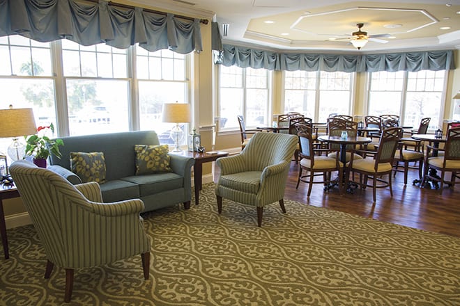 A cozy living area featuring a sofa, chairs, and tables with large windows and decorative curtains.