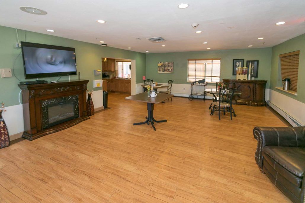 A spacious living area with wooden flooring, featuring a television, furniture, and dining tables.
