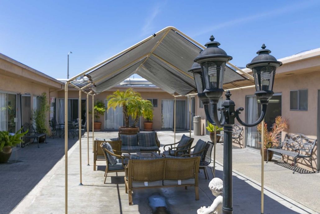 A cozy outdoor patio with a gazebo, seating area, and decorative lamp posts on a sunny day.