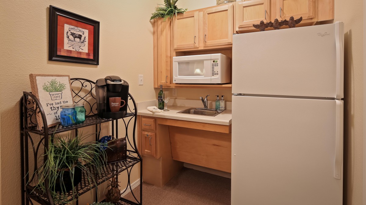 A compact kitchen area featuring a microwave, refrigerator, and sink with wooden cabinets.
