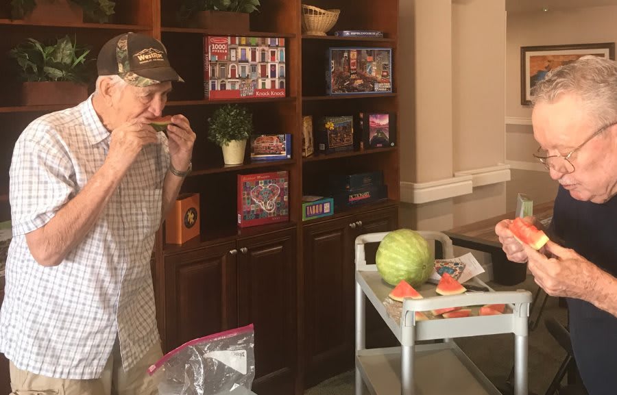 A man indoors eating a slice of watermelon next to shelves filled with items.