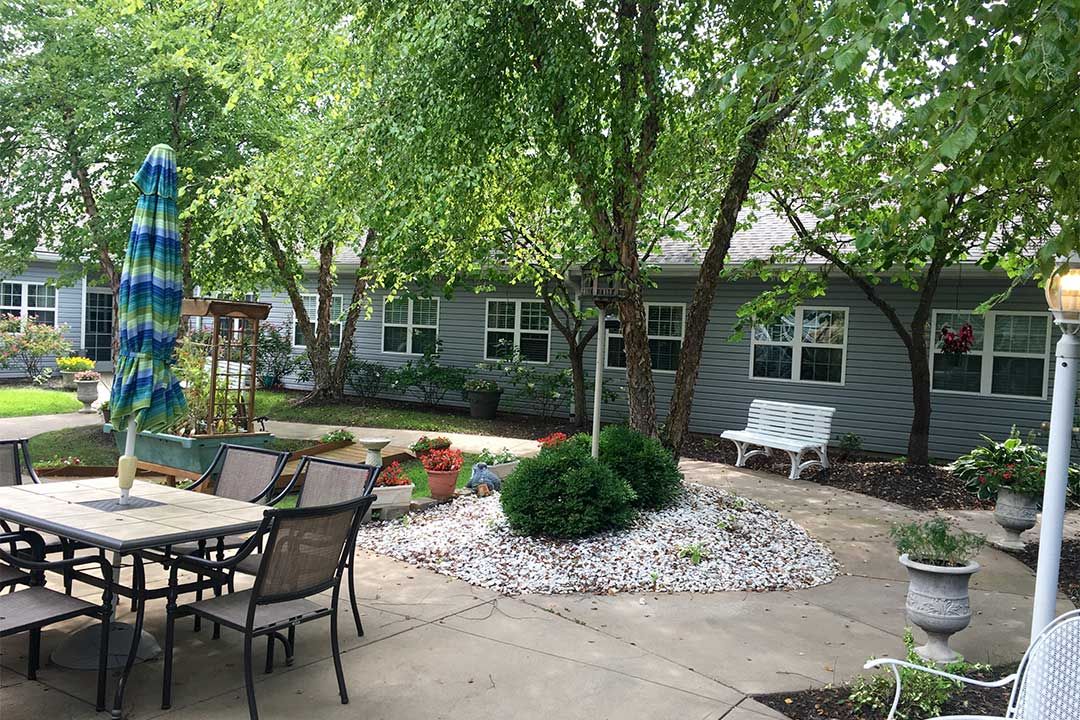 A tranquil backyard patio with trees, outdoor furniture, and a landscaped garden area.