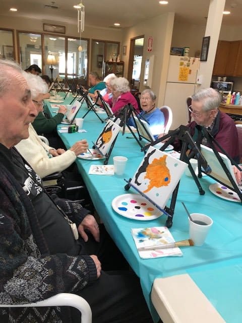 A group of seniors participating in an art class, painting on canvases with vibrant colors.