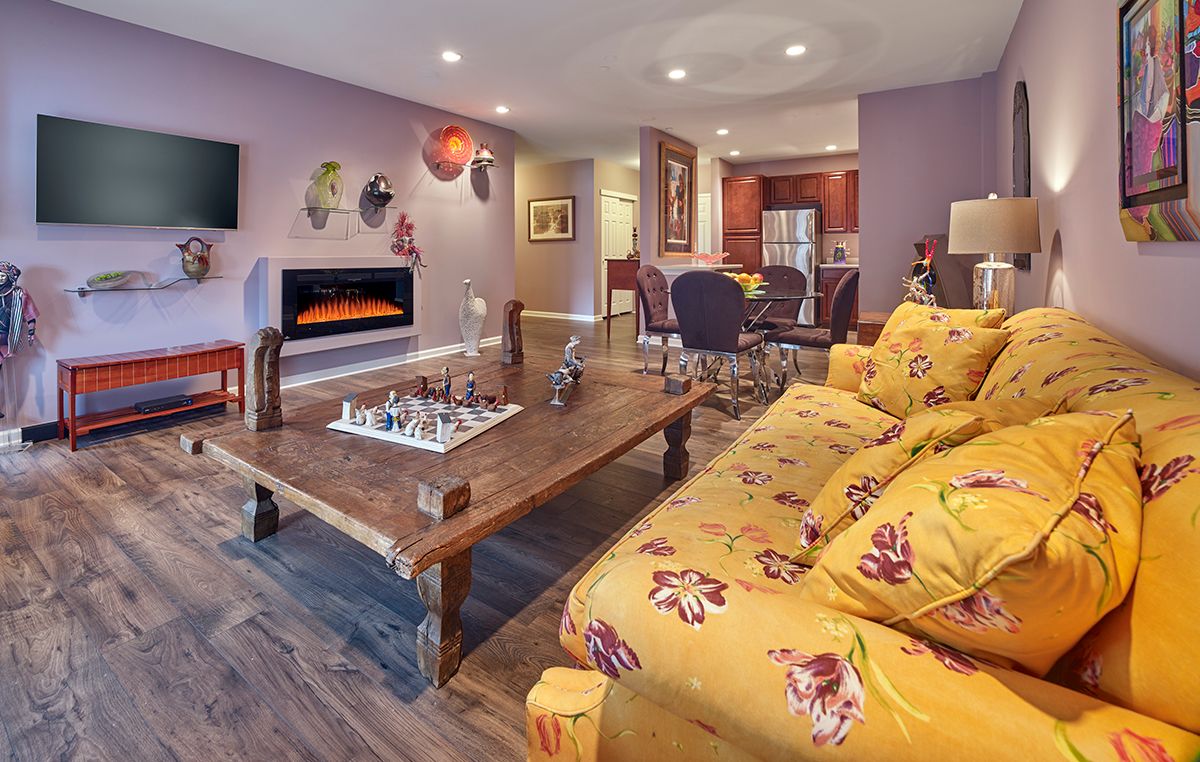 A cozy living room with a colorful sofa and chess board on a wooden table, featuring an open concept layout with a fireplace.