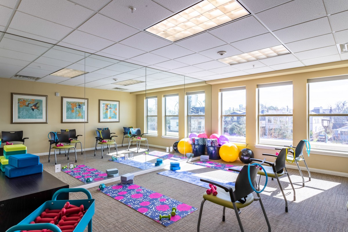 A brightly lit exercise room with yoga mats, fitness equipment, and mirrors.