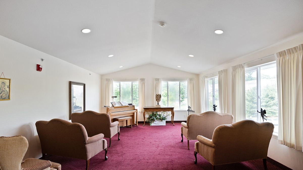 A spacious living room with a red carpet, featuring elegant couches and a piano by large windows.