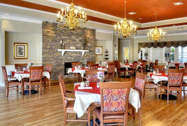 An elegant restaurant dining area featuring neatly arranged tables and chairs, chandeliers, and a stone fireplace.