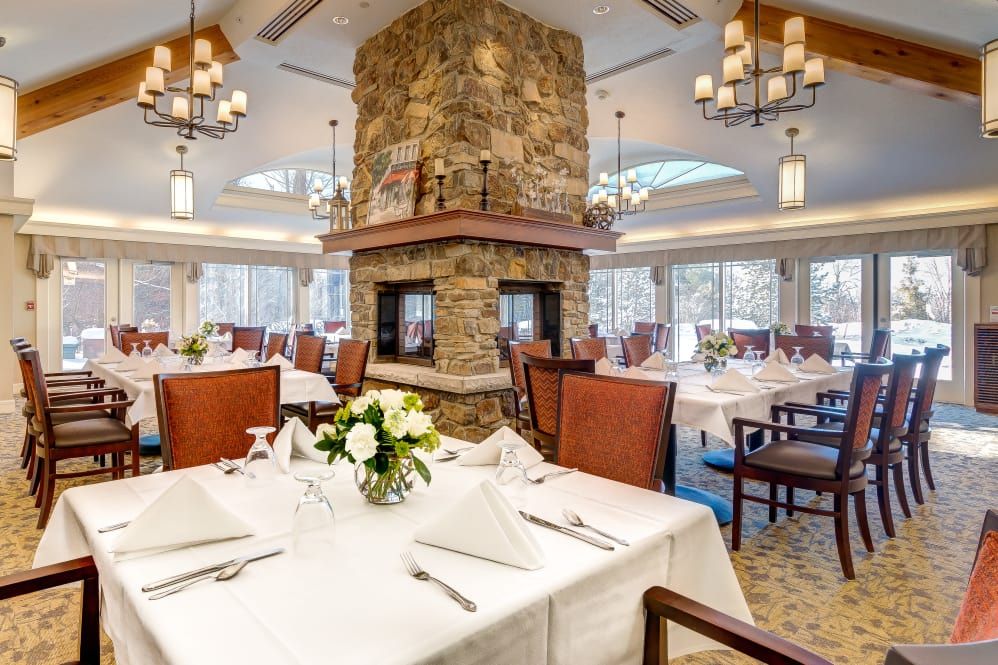 A formal restaurant dining room with a large stone fireplace and elegant table settings.