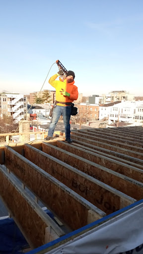 A construction worker on a roof, using a tool while wearing safety gear.