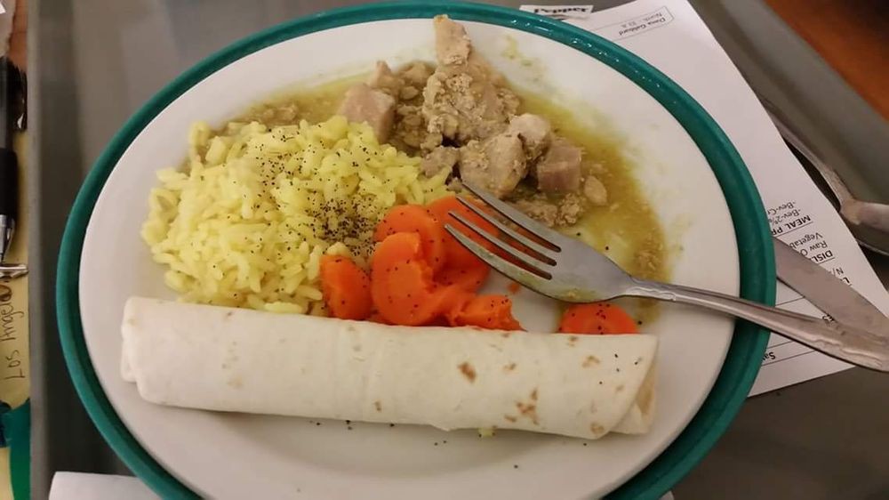 A plate of food featuring chicken, yellow rice, carrots, and a tortilla.