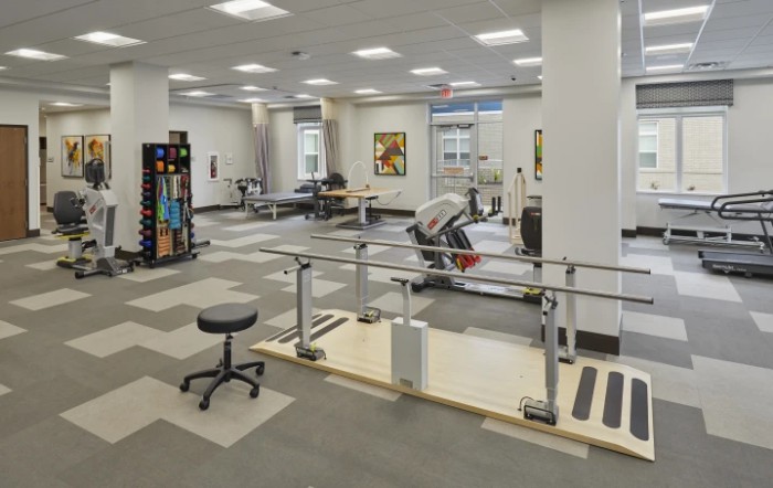 A spacious rehabilitation center with various exercise equipment and parallel bars for physical therapy.