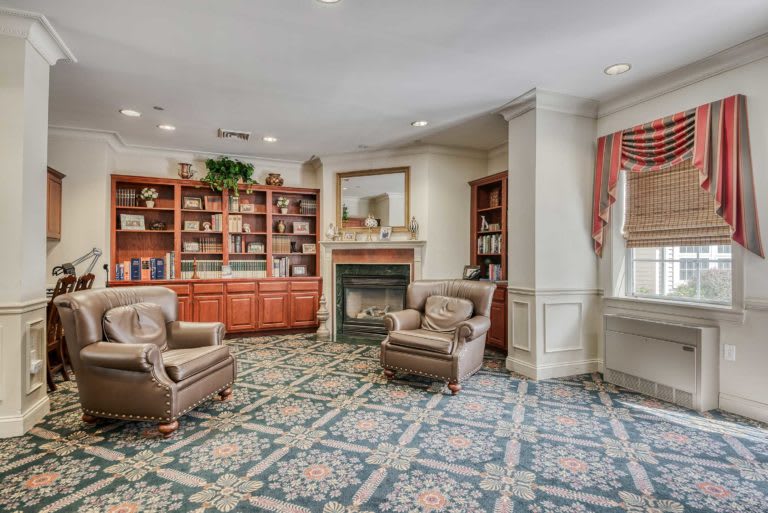 A cozy library with bookshelves, armchairs, and a fireplace.