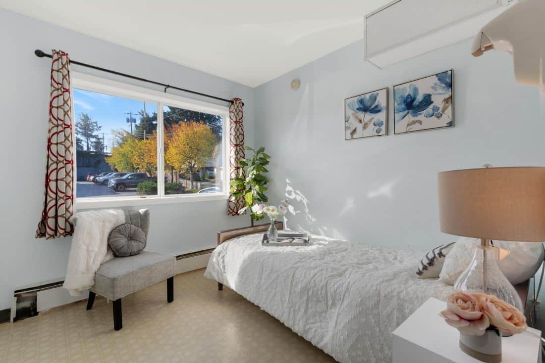 A modern, minimalist bedroom with a large window letting in natural light, featuring simple decor and a touch of greenery.