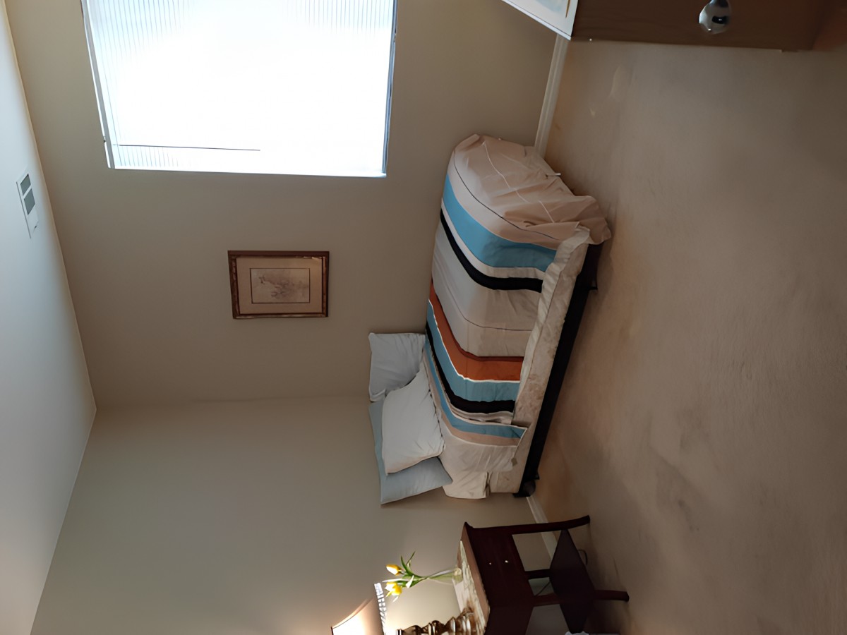 A minimalist bedroom with a neatly made bed, a window allowing natural light, and simple decor.