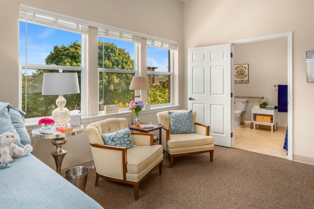 A cozy living room with sunlight streaming through large windows, featuring comfortable chairs and elegant decor.