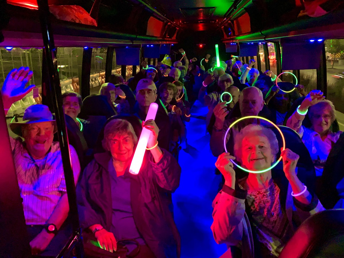 A group of seniors enjoying a lively party bus ride with glow sticks and colorful lights.