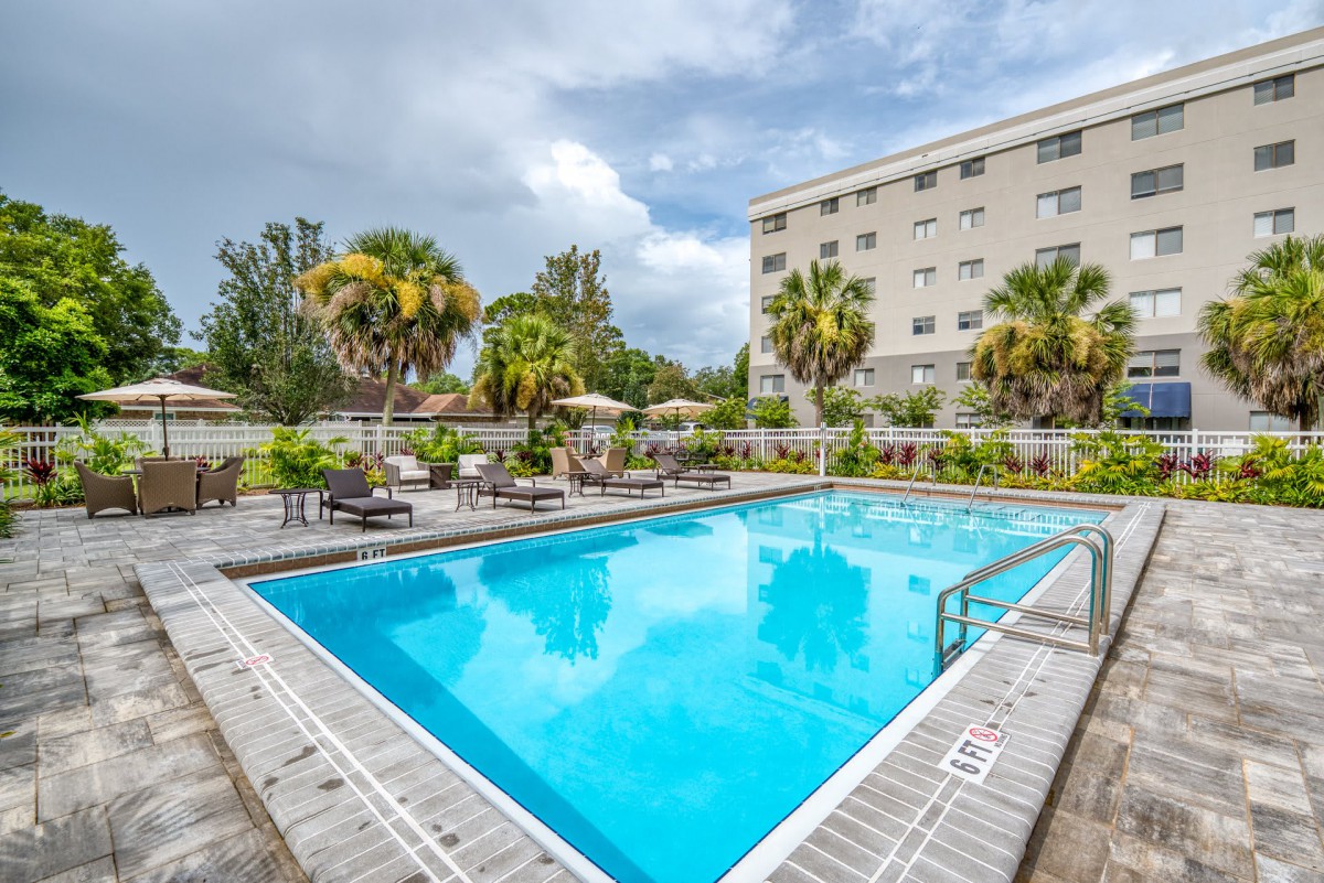 An inviting outdoor swimming pool area surrounded by palm trees and lounge chairs at a hotel.